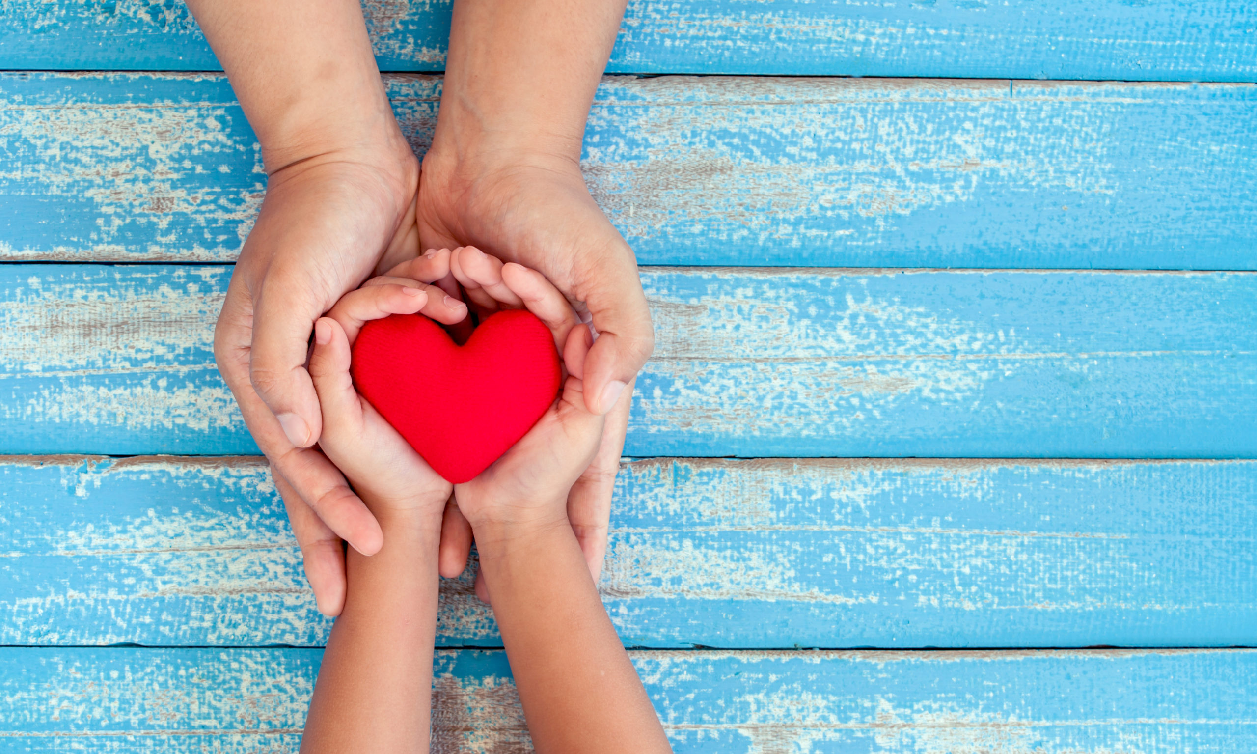 Kinderhand und Erwachsenenhand halten symbolisches Herz